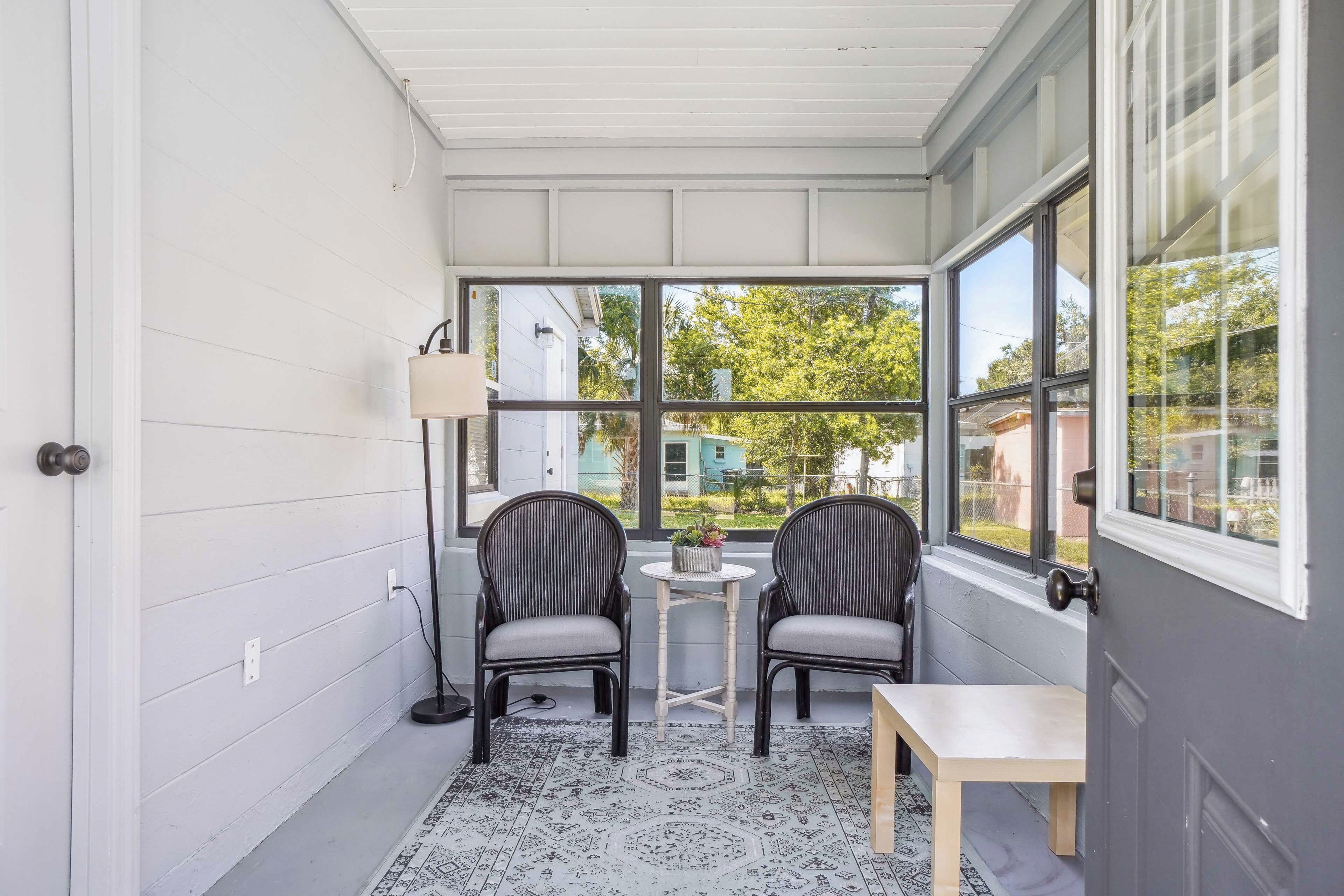 A covered porch with two chairs, a small table, and a lamp.