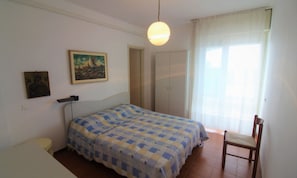 Un dormitorio con dos camas, una silla, un cuadro, una puerta y una ventana con cortinas.