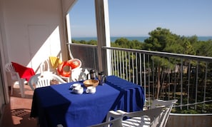 A balcony with a table set for two, a chair, a red towel, and a life preserver.