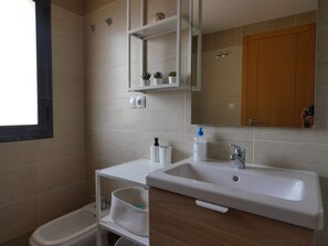 Un baño con un lavabo blanco, un espejo, un mueble de madera y un pequeño estante con plantas.