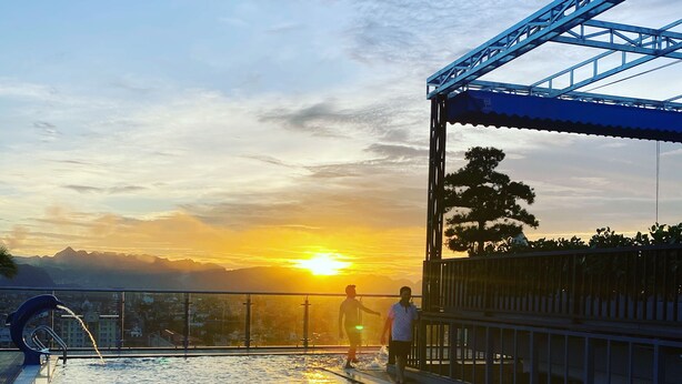 An outdoor swimming pool with a view of the sunset and mountains in the background. - Riverside Hotel Ha Nam (Phu Ly)