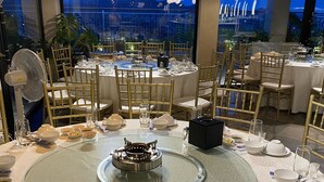 A restaurant with round tables, gold chairs, and a central stove. - Riverside Hotel Ha Nam (Phu Ly)