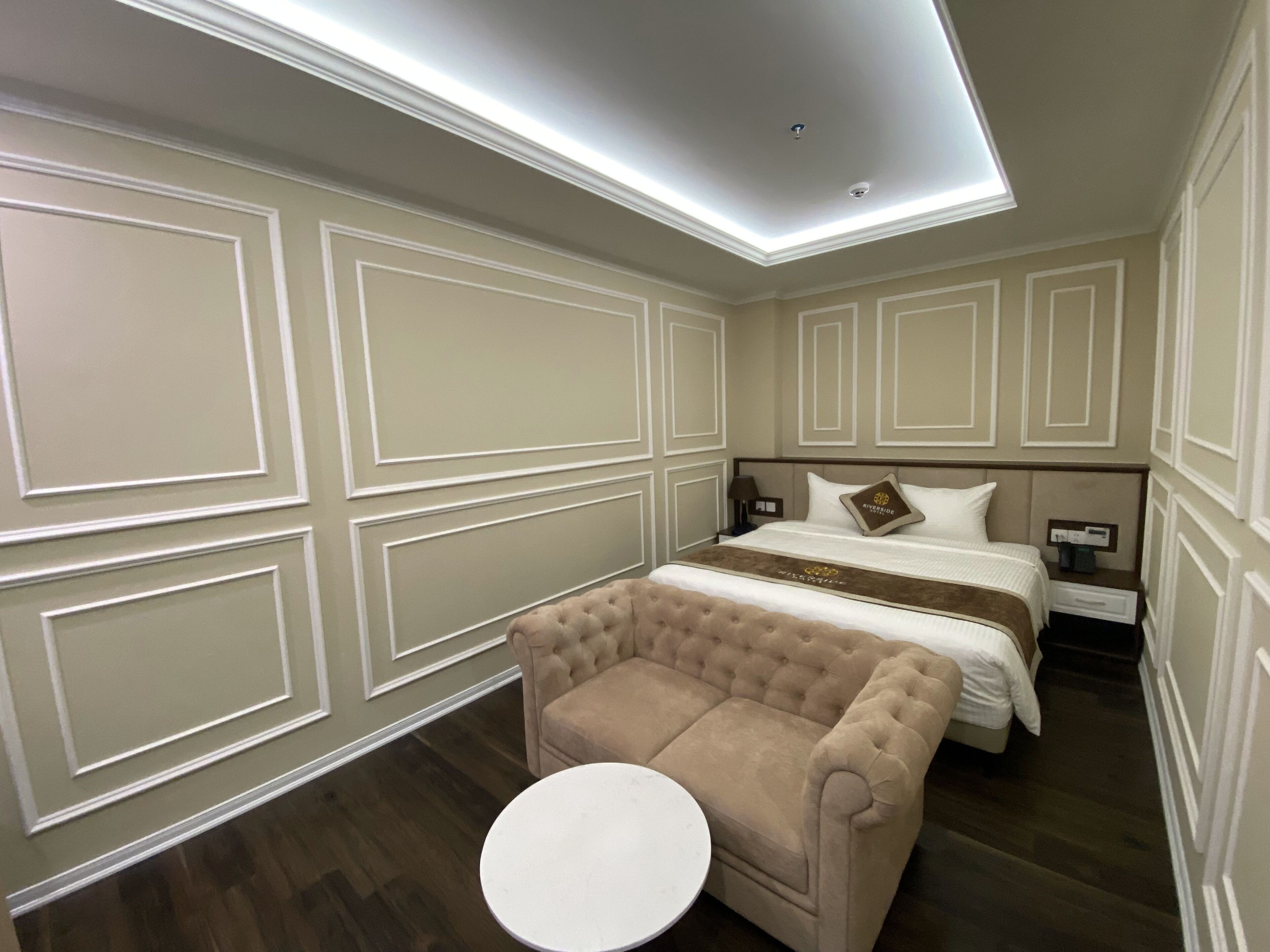 Una habitación de hotel con una cama grande, un sofá, una mesita redonda y una mesita de noche.