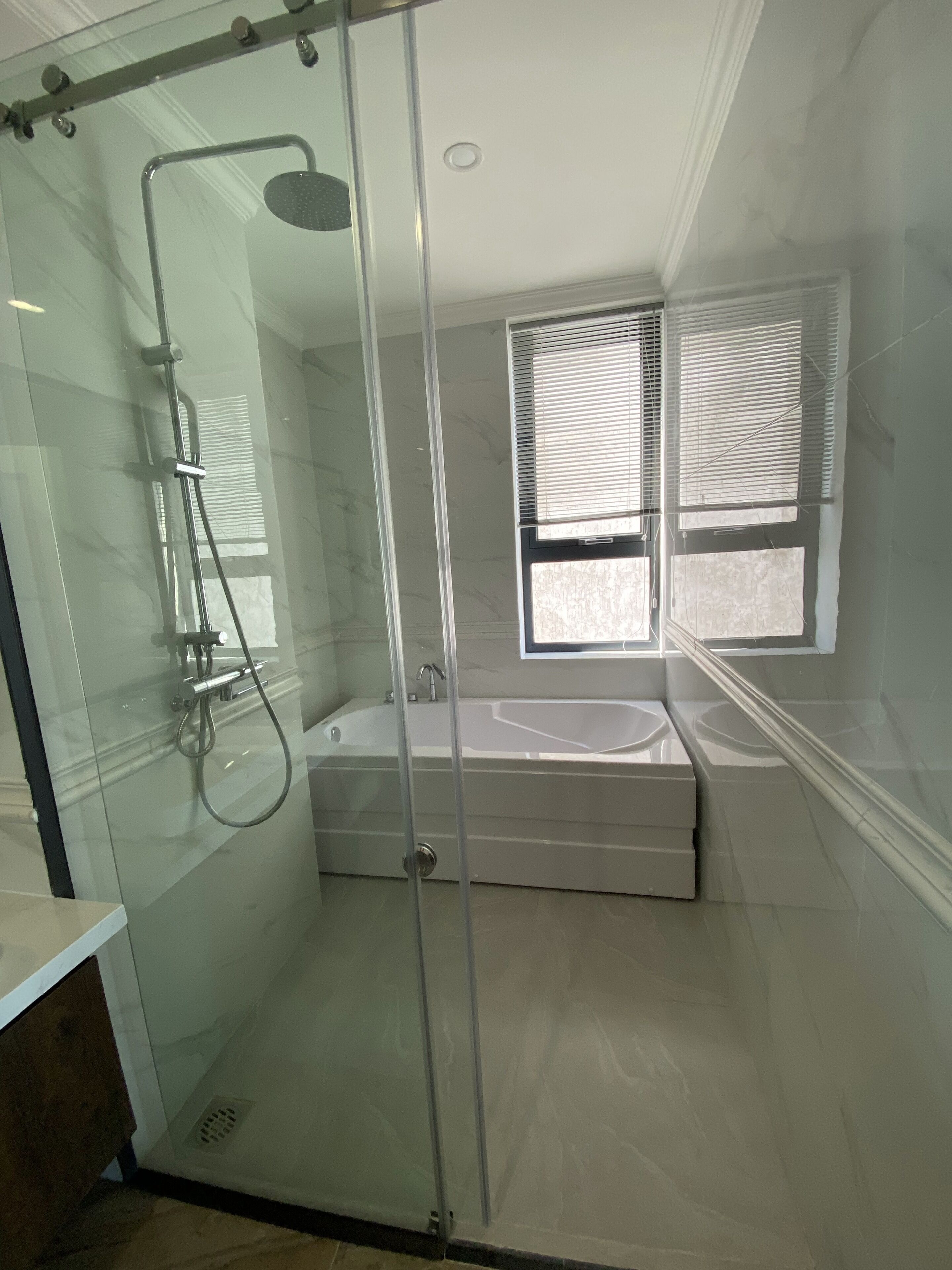 A modern bathroom with a glass-enclosed shower, a bathtub, and a window with blinds.