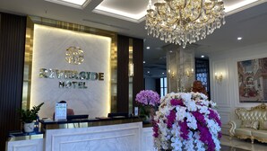 A hotel reception area with a marble reception desk, a chandelier, and a large floral arrangement. - Riverside Hotel Ha Nam (Phu Ly)
