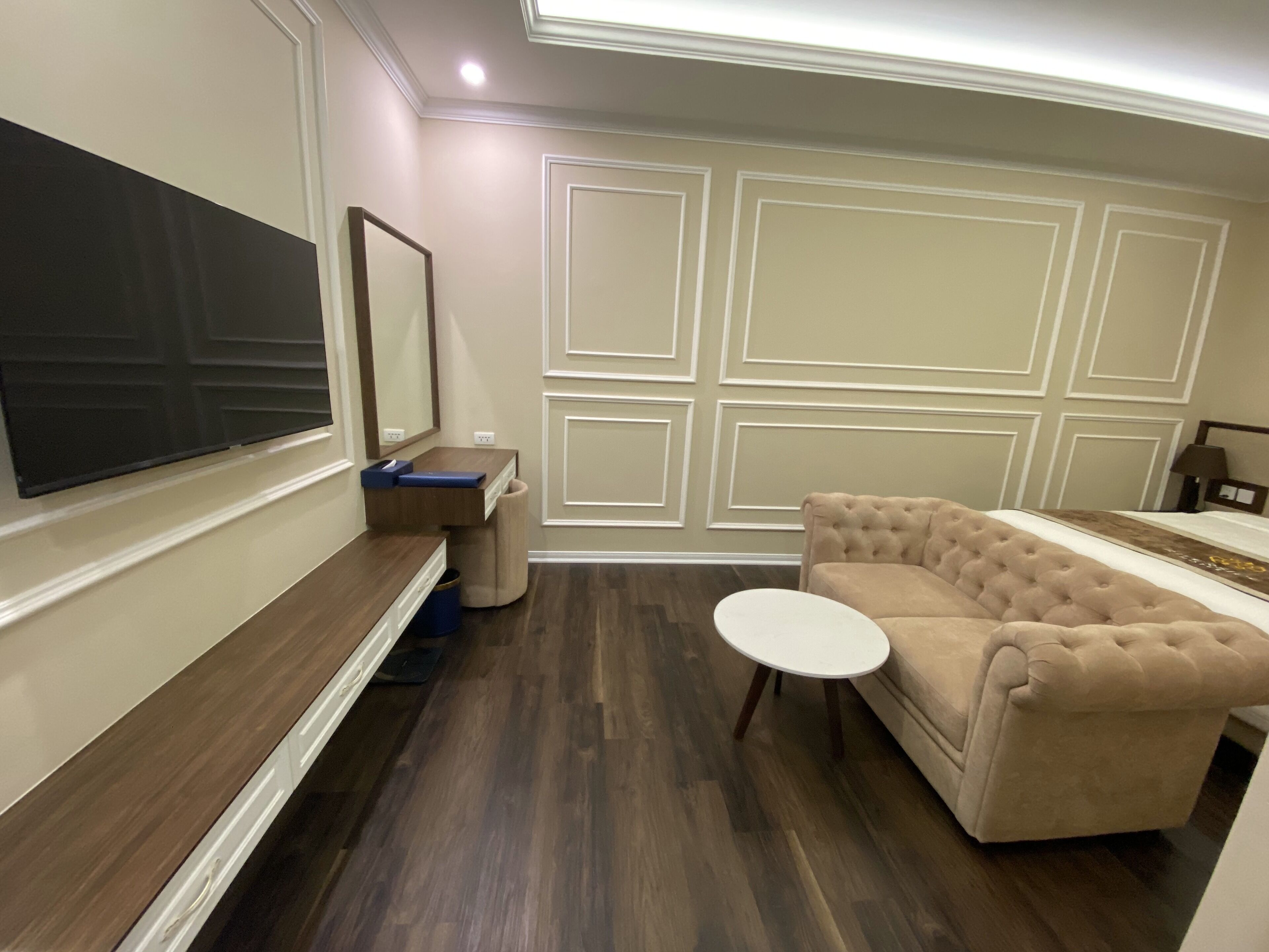 Una sala moderna con un televisor de pantalla plana grande, un sofá color beige, una mesita de centro redonda y un mueble empotrado con espejo.