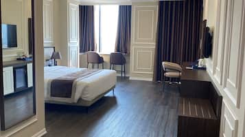 Une chambre d’hôtel avec un grand lit, un bureau, deux chaises, une télévision et une salle de bain avec un miroir.