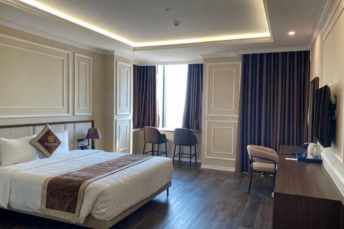 Habitación de hotel con una cama grande, dos sillas, un escritorio, un televisor de pantalla plana y un ventanal con cortinas.