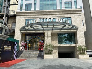 The Riverside Hotel entrance with a grand opening sign, marble facade, and a glass canopy over the entrance.