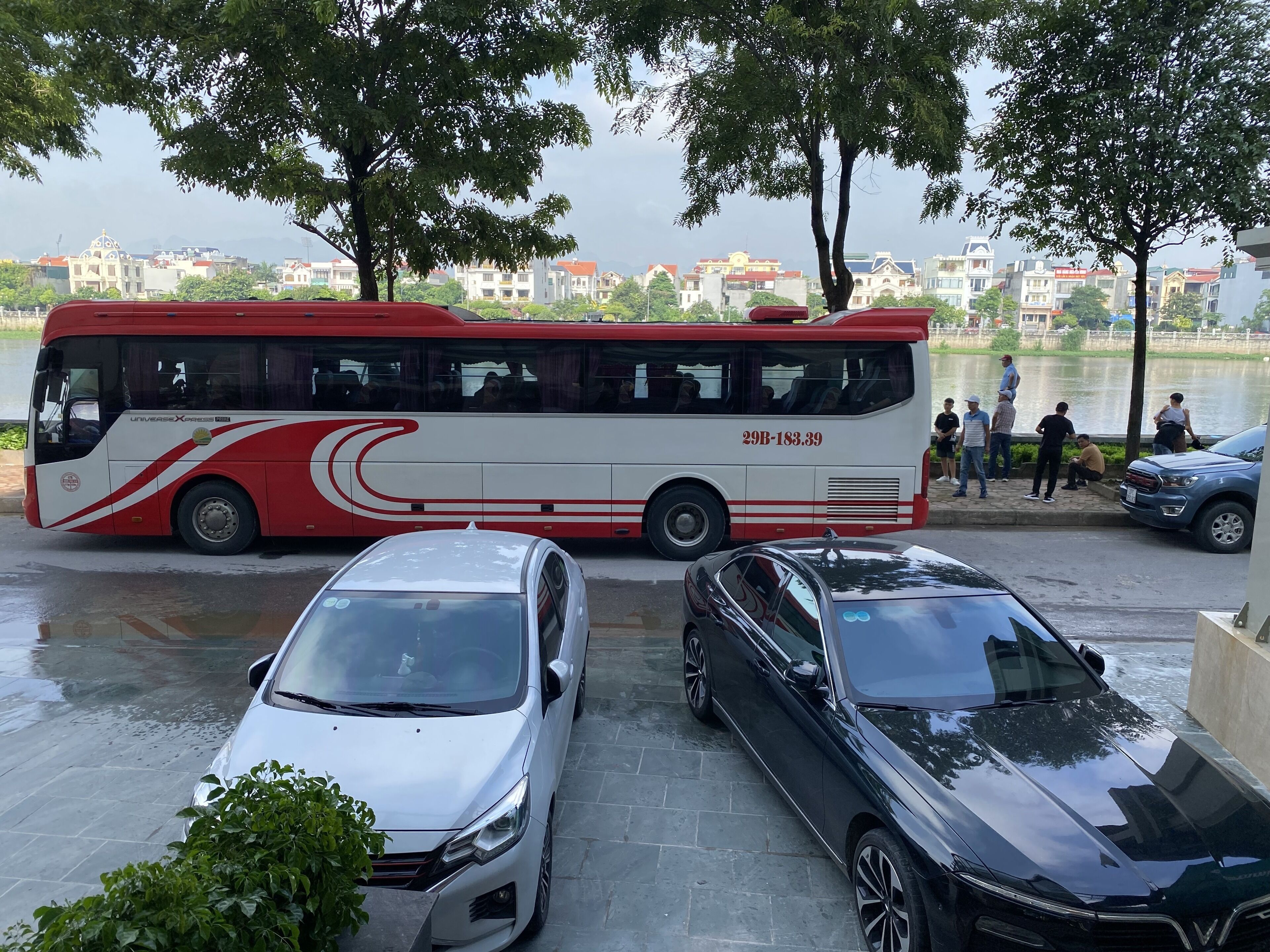 Un autobús rojo y blanco estacionado cerca de un cuerpo de agua, con una fila de coches adelante.