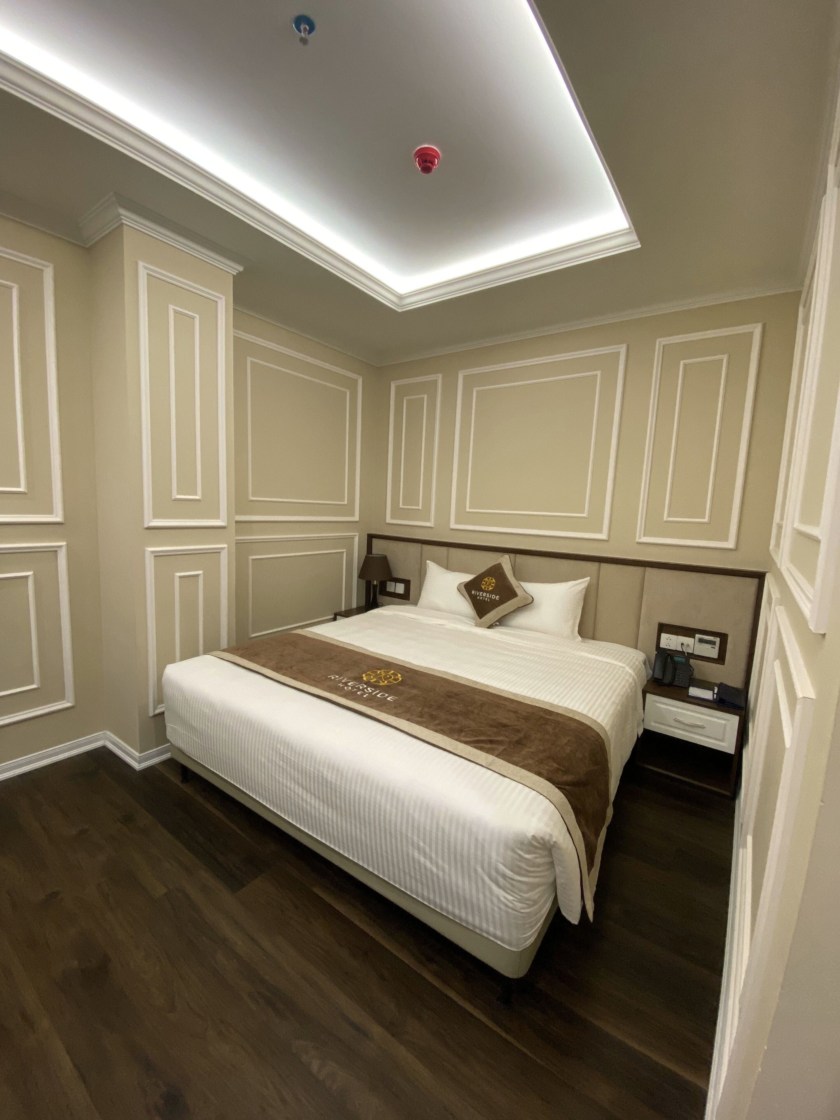 A hotel room with a large bed, a nightstand, a lamp, and a ceiling light.