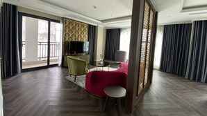 A spacious hotel room with a large balcony, a flat-screen TV, a green armchair, a red sofa, and a small round table. - Riverside Hotel Ha Nam (Phu Ly)