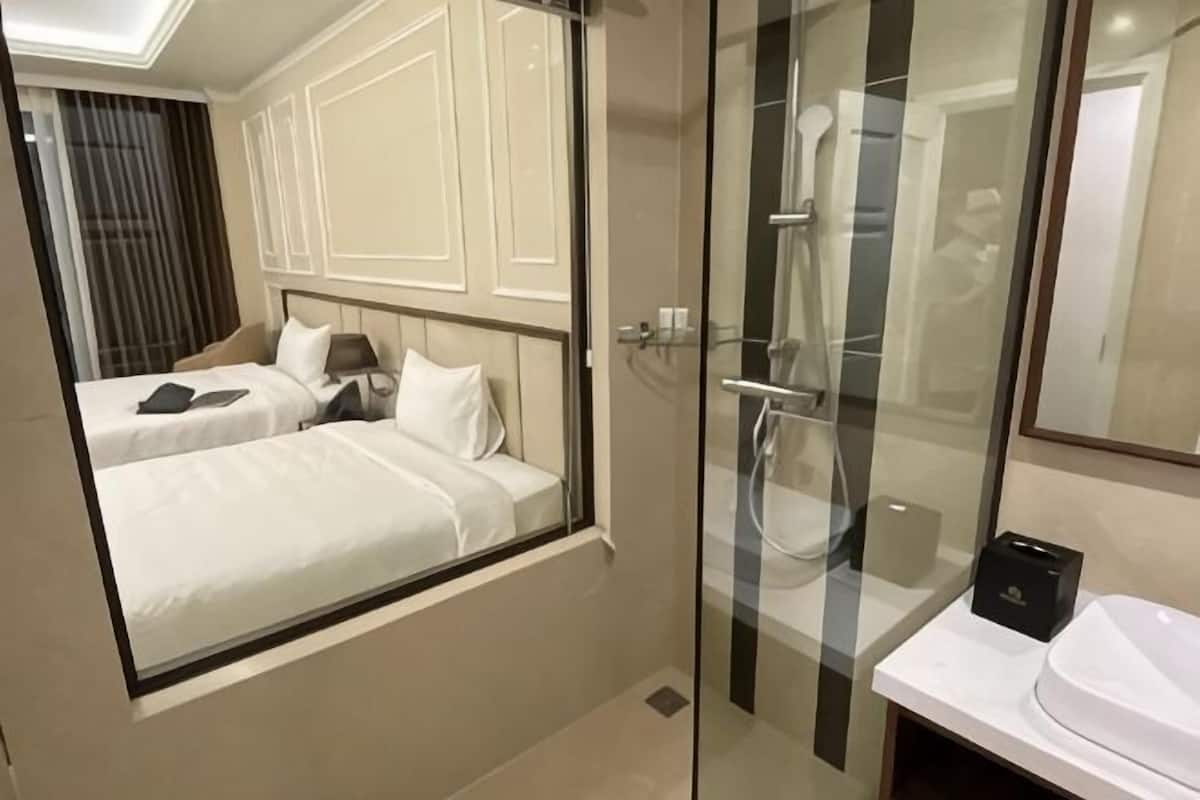 Una habitación de hotel con una cama, cabina de ducha de vidrio y un lavamanos blanco.