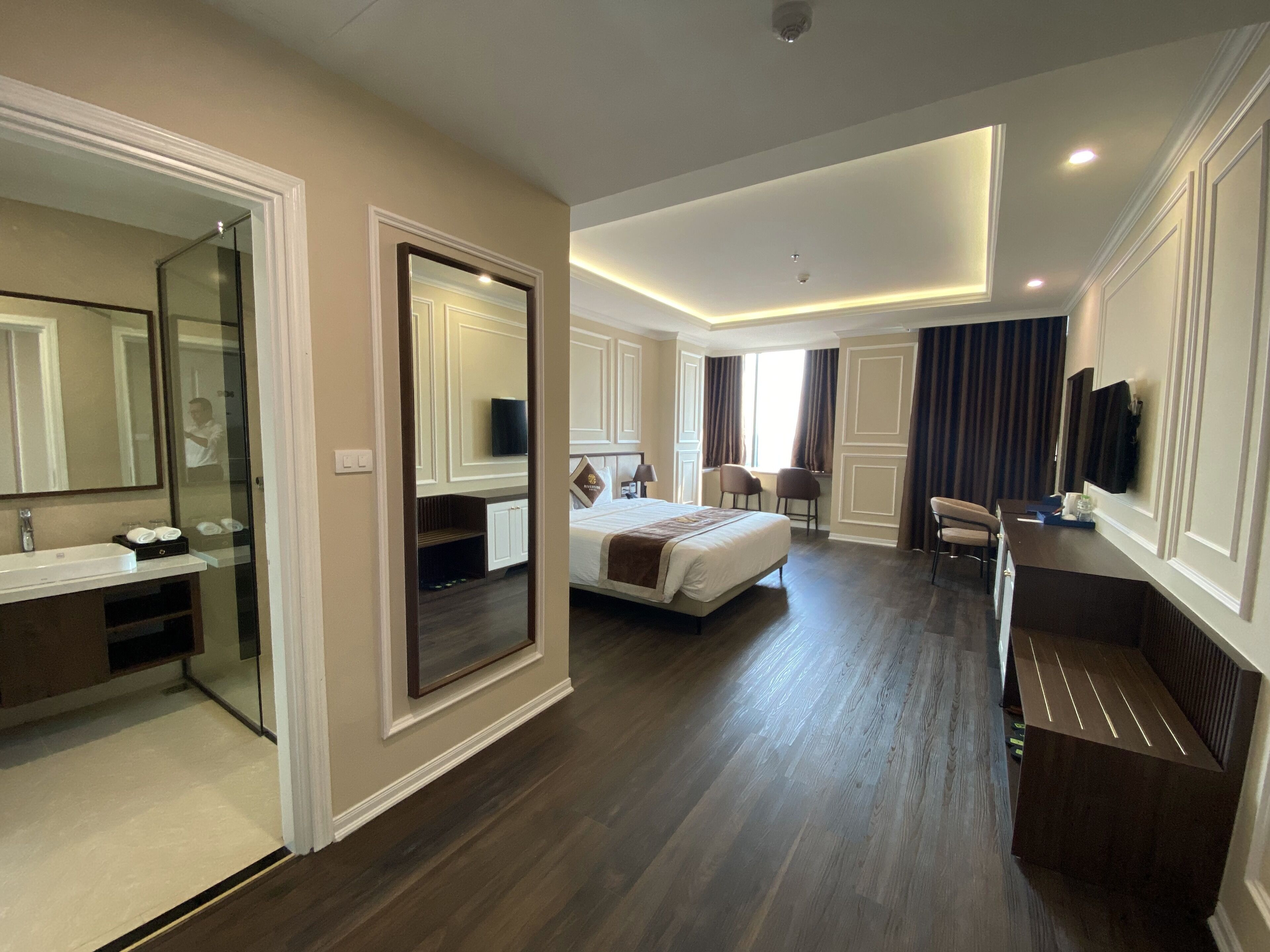 A hotel room with a large bed, a desk, a chair, a TV, and a mirror.