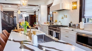 A modern kitchen with a marble island, stainless steel appliances, and a chandelier.