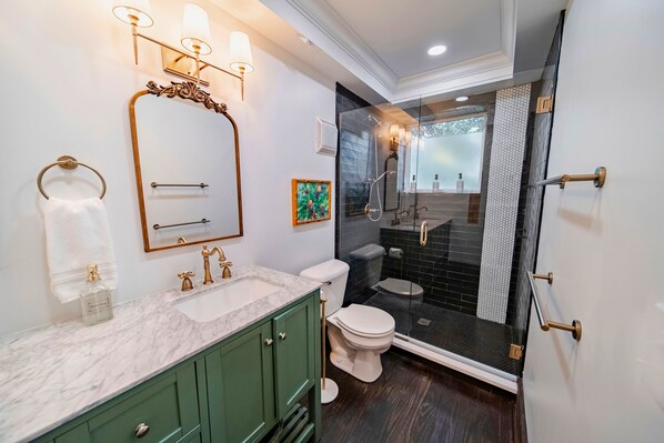 A modern bathroom with a marble sink, green cabinets, a white toilet, and a glass-enclosed shower.