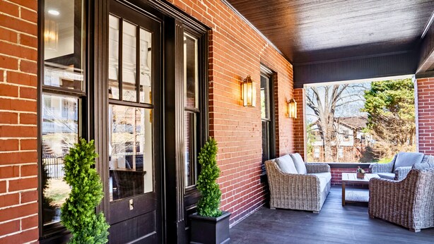 A covered outdoor seating area with wicker furniture and a view of a tree and house.