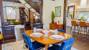A dining area with a wooden table set for four, blue upholstered chairs, and a staircase leading to another level.