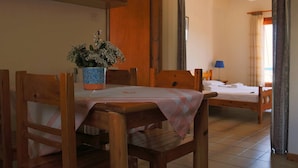 A room with a wooden dining table, a bed, and a window with curtains. - Seaview - Selfcatering Apartment - Helen No 1 (North Kynouria)