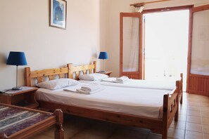 A room with two wooden beds, a small table, two lamps, a framed picture on the wall, and a door leading outside. - Seaview - Selfcatering Apartment - Helen No 1 (North Kynouria)
