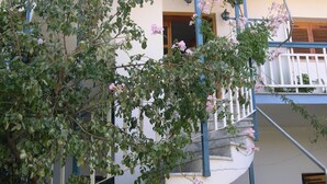 A building with a white facade, a blue balcony, and a tree with pink flowers. - Seaview - Selfcatering Apartment - Helen No 1 (North Kynouria)