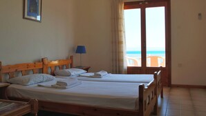 A room with two wooden beds, a framed picture on the wall, a lamp, and a view of the sea through a door. - Seaview - Selfcatering Apartment - Helen No 1 (North Kynouria)