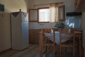 Uma cozinha com geladeira, armários de madeira, uma janela com cortinas e uma mesa de jantar com cadeiras.