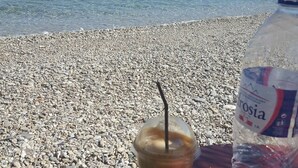 A table with a plastic cup of iced coffee, a bottle of water, and a clear view of the sea and distant boats. - Seaview - Selfcatering Apartment - Helen No 1 (North Kynouria)