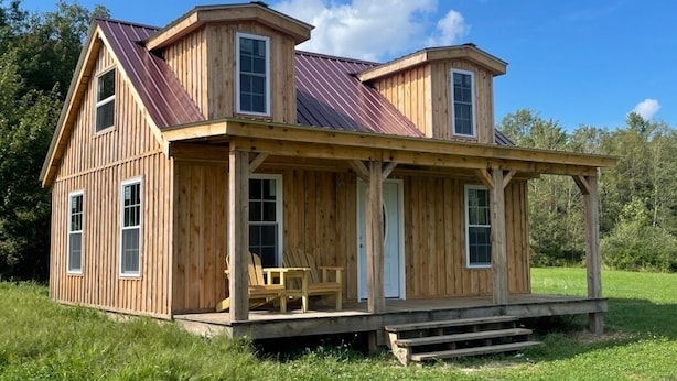 Una baita di legno con veranda, due camere da letto e un'ampia finestra fronte.