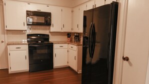 A kitchen with white cabinets, a black refrigerator, a stove, and a microwave. - Quiet, 4-bed home with a park view. (Clarksville)