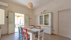 Un coin repas avec une table dressée pour quatre personnes, entouré de chaises colorées, d’un meuble avec des portes en verre et d’un luminaire suspendu.