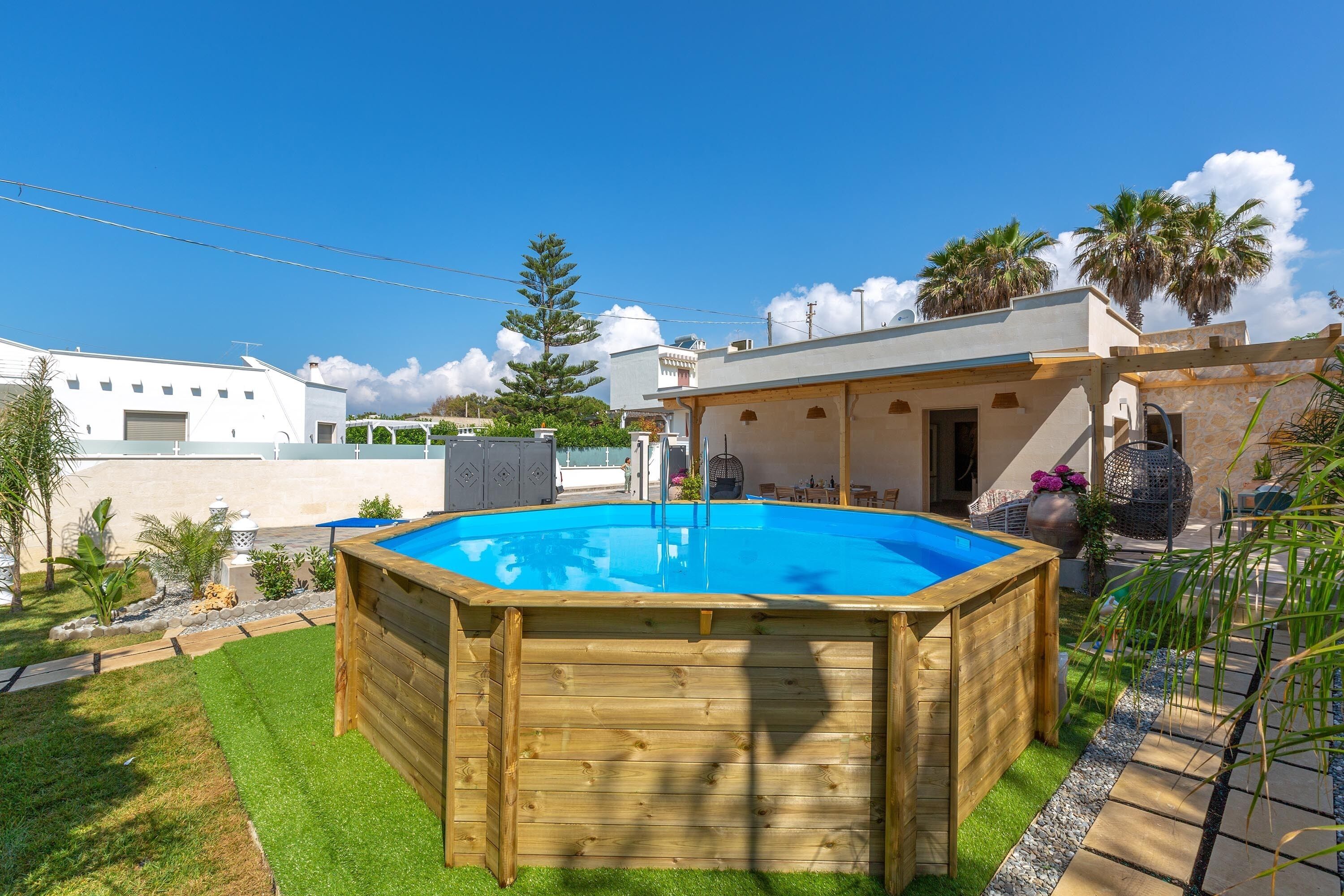 Ein hölzerner Pool, umgeben von einem Garten mit einem kleinen Haus im Hintergrund.