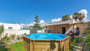 Une piscine en bois, entourée d’un jardin, avec une petite maison en arrière-plan.