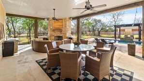 Un patio al aire libre con una mesa redonda y sillas de mimbre, una chimenea de piedra y vistas a una piscina.
