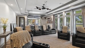Amplia habitación con varios sofás y sillones de cuero, ventilador de techo y ventanas amplias que ofrecen vistas al exterior.