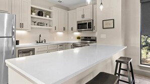Una cocina moderna con armarios blancos, electrodomésticos de acero inoxidable e iluminación colgante.