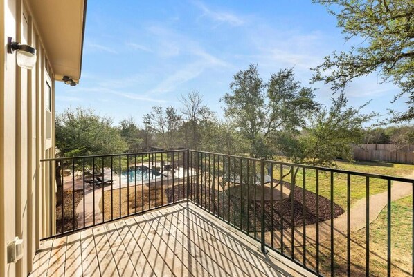 A wooden deck with a metal railing, a swimming pool, and a landscaped yard with trees and a wooden fence.