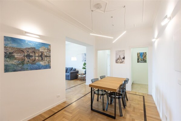 A modern dining area with a wooden table and chairs, a painting on the wall, and a view into another room.