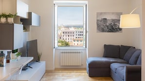 A modern living room with a large window, a grey sofa, a flat-screen TV, and a minimalist design.