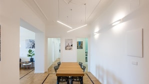 A modern conference room with a wooden table and chairs, white walls, and a herringbone floor pattern.