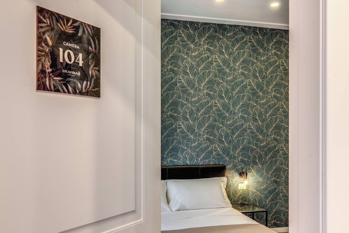 A bedroom with a bed, a nightstand, and a wall-mounted light.