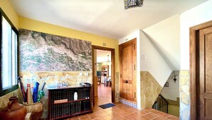 Un couloir doté d’un sol carrelé, un comptoir d’accueil avec divers objets, une grande peinture abstraite et un escalier avec des murs en pierre.