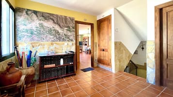 Un pasillo con suelo de baldosas, una recepción con diversos objetos, un cuadro abstracto de gran tamaño y una escalera con paredes de piedra.
