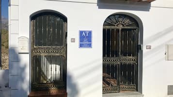 Un edificio con dos puertas negras ornamentadas, un letrero azul con 'AT' y '1A' que indica números de apartamentos, y un buzón pequeño a la izquierda.