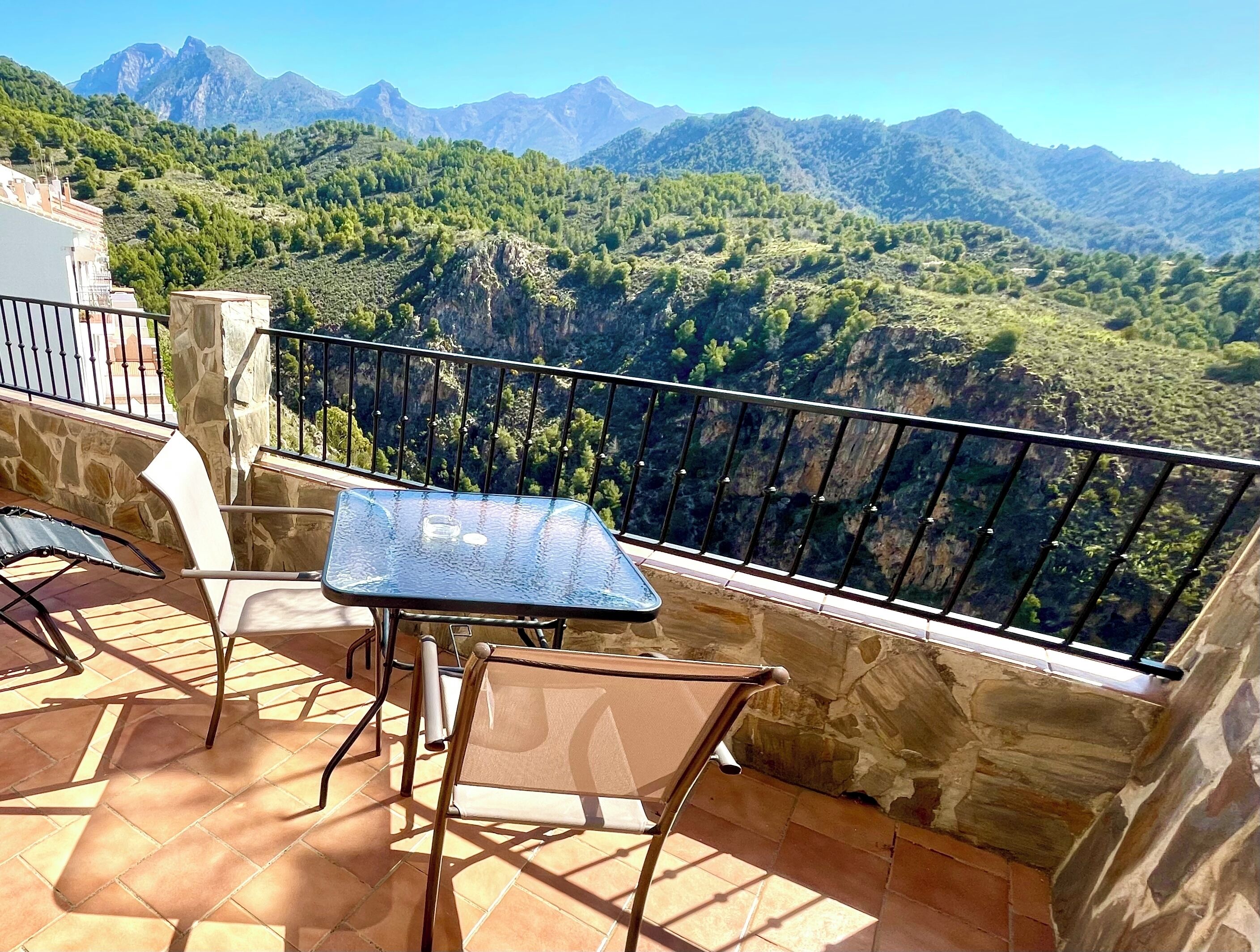 Una terraza con mesa y sillas, muros de piedra y vistas a montañas.