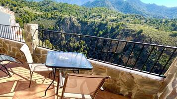 Una terraza con mesa y sillas, muros de piedra y vistas a montañas.