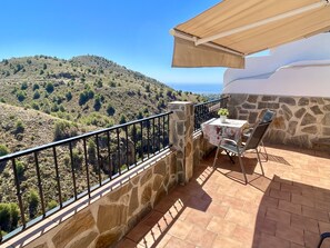 Un balcon aux murs en pierre, une table avec des chaises et une vue sur un paysage vallonné.