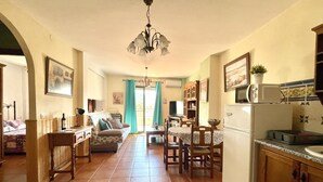 Un salon confortable avec un canapé, une table à manger et des chaises, une cuisine équipée d’un réfrigérateur et d’un four à micro-ondes, et un coin repas offrant une vue sur l’extérieur.