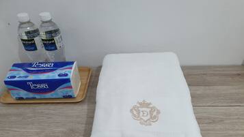 Una mesa de madera con una toalla blanca doblada que presenta un monograma, una caja de pañuelos Tessa y dos botellas de agua.