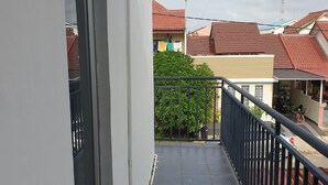 Ein schmaler Balkon mit schwarzem Geländer, Fliesenboden und Blick auf Nachbarhäuser mit roten Dächern.